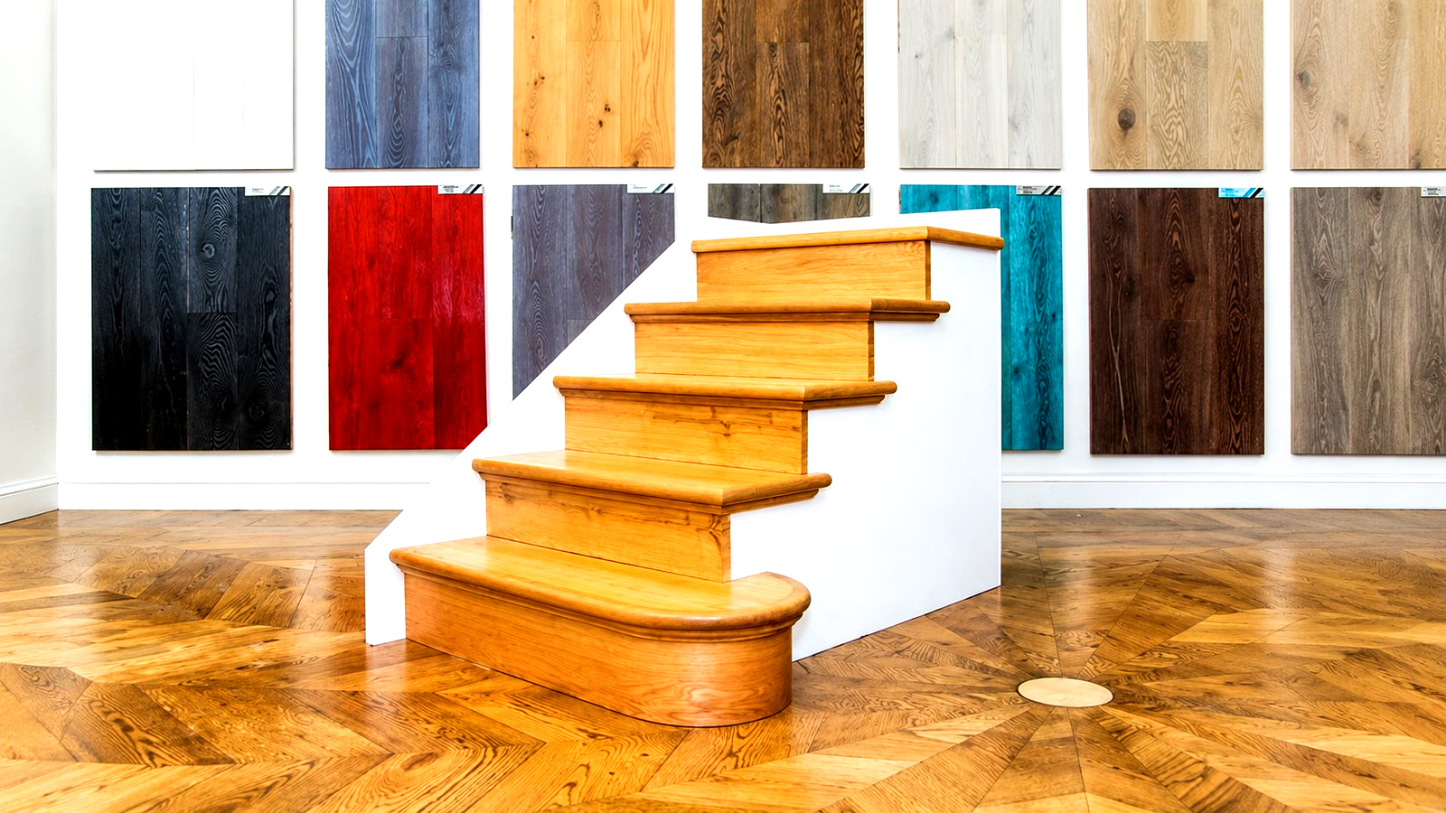 The Timberzone Studio showroom — finished oak staircase set against the colour-sample wall and Versailles parquet floor