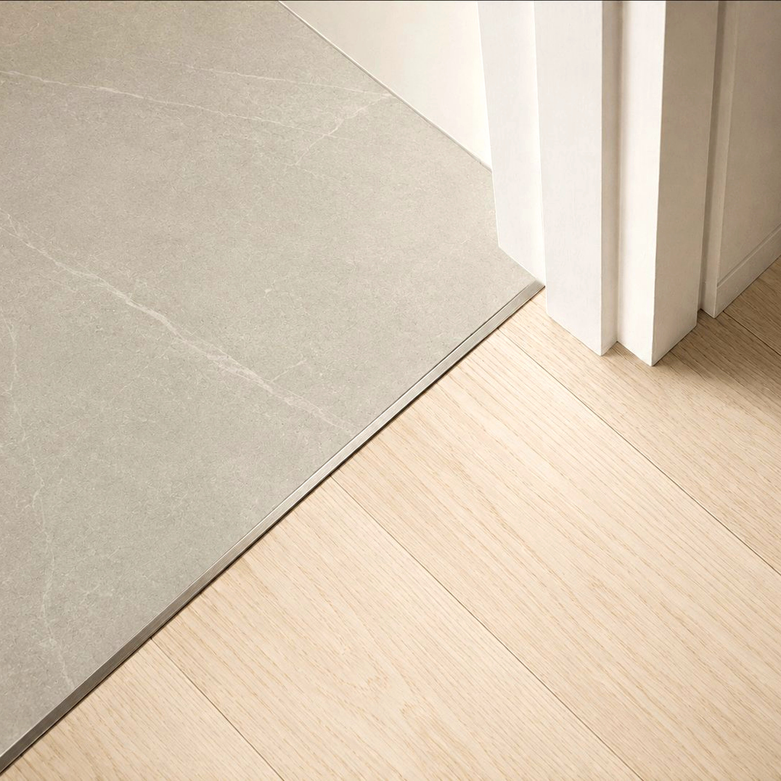 Stainless steel threshold joining pale oak to grey stone tile — Timberzone Studio bespoke detail