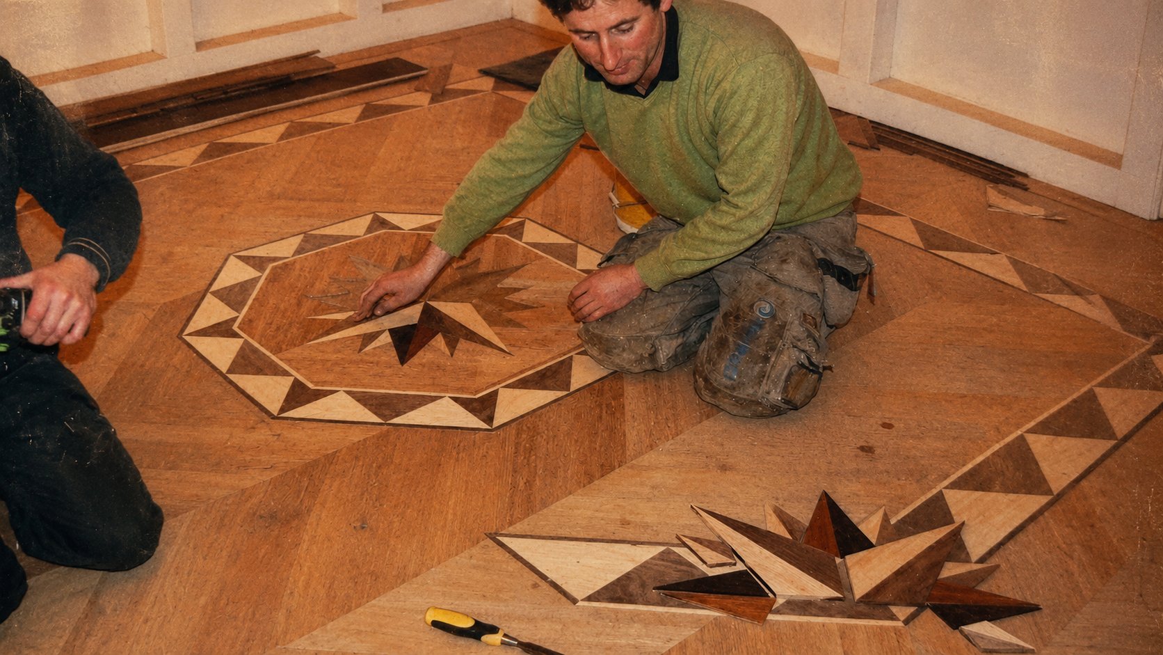 Two craftspeople hand-fitting a bespoke parquet inlay — Timberzone Studio installation team at work